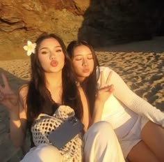 two women sitting on the beach making peace signs