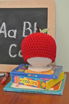 a crocheted apple sitting on top of books next to a chalkboard with writing