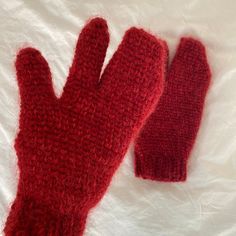 two red knitted mittens laying next to each other on a white sheet,