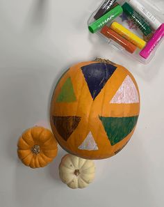 an orange painted pumpkin sitting on top of a table next to markers and crayons