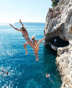 two women jumping into the water from cliffs to cliff face each other with their arms in the air