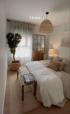 a bedroom with a bed, table and lamp on the side of the room in front of a window