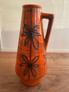 an orange vase sitting on top of a wooden table