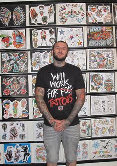 a man with tattoos standing in front of a wall full of stickers on it