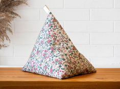 a triangle shaped pillow sitting on top of a wooden table next to a potted plant