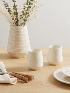 the table is set with white dishes, silverware and a vase filled with flowers