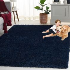 a young boy laying on top of a blue rug next to a large brown dog