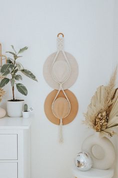 three hats hanging on the wall next to a potted plant and vase with flowers