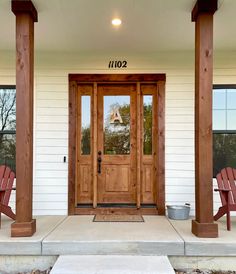 two red chairs sitting on the front porch of a white house with wood columns and doors