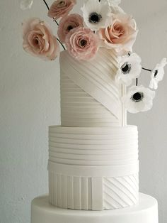 a three tiered white cake with pink and white flowers on the top, along with black and white stripes