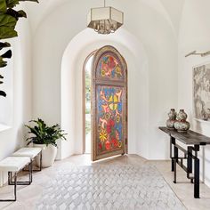 an arched entryway with artwork on the wall and table in front of it, along with potted plants