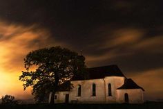 an old church with a tree in front of it under a cloudy sky at night