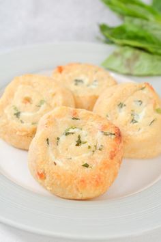 four small biscuits on a white plate next to some green leaves