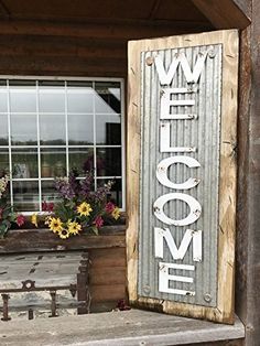 a welcome sign on the side of a building next to a bench with flowers in it