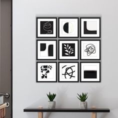 black and white artwork on the wall above a table with two potted plants in front of it