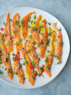 a white plate topped with sliced up salmon on top of a blue table cloth and garnished with herbs