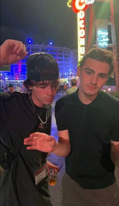 two young men standing next to each other in front of a neon sign at night