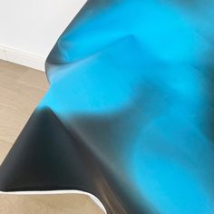 an abstract blue and black sculpture sitting on top of a hard wood floor next to a white wall