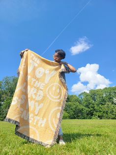 a woman standing in the grass holding a yellow and white blanket that says love is everywhere