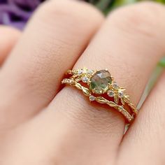 a close up of a person's hand with a ring on their finger and flowers in the background