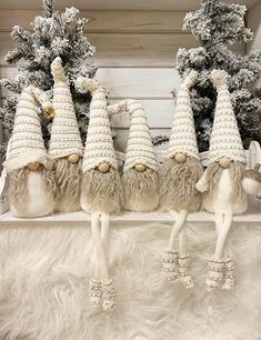 four knitted gnomes are lined up in front of some fake trees and pine cones