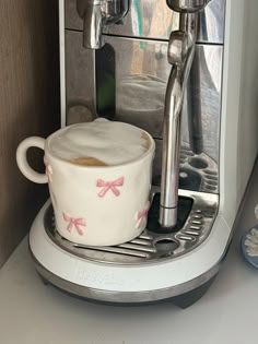 there is a coffee cup with pink bows on it and the espresso machine in the background