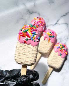 three ice cream cones with sprinkles on them sitting on top of black gloves