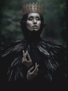 a woman wearing a crown with feathers on her head and hands in front of her face