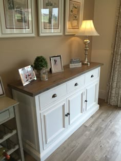 a white dresser with two pictures on it and a lamp in front of the dresser