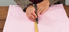 a person is measuring the length of a pink piece of fabric with a ruler in their hand