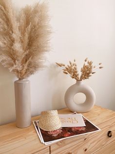 there is a hat on the table next to a vase with dry grass in it