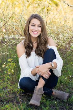 a woman sitting in the grass with her legs crossed and looking at the camera, smiling