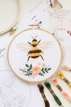 a cross stitch bee sitting on top of a table next to some scissors and thread