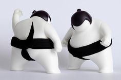 two white plastic figurines with black straps on their backs, facing each other