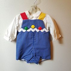 "- This great vintage outfit by C.I. Castro and Co. is perfect for any occasion. The romper is blue and white striped with one red strap and one yellow strap. It is fully lined and buttons at back and snaps between legs. The front is detailed with a giant white rick rack trim and 3 plastic fish buttons. The back has large red buttons. The shirt underneath is white and long sleeved with buttons down back. Size is: 12 months Length: 15\"	in stock	34.65 USD	"	3.50 USD	Clothing > Boys' Clothing > Ba Long Sleeve Cotton Overalls With Buttons, Cotton Overalls With Sleeves And Buttons, Retro Cotton Fitted Jumpsuits And Rompers, Vintage Blue Cotton Overalls, Fitted Cotton Jumpsuits And Rompers For Playtime, Fitted Cotton Overalls With Buttons, Vintage Blue Long Sleeve Overalls, Playful Blue Cotton Jumpsuits And Rompers, Blue Cotton Playful Jumpsuits And Rompers