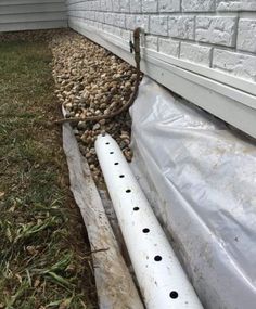 a white pipe laying on top of a grass covered ground next to a building with rocks in it