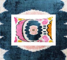 a blue, pink and yellow pillow with a white square in the middle on a rug