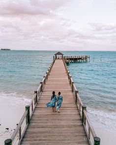 two women walking down a pier towards the ocean