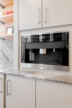 the microwave is built into the wall in the kitchen with marble counter tops and white cabinets