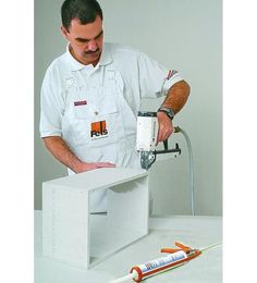 a man in white shirt using a power tool on a piece of construction material with tools nearby