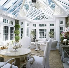 a living room filled with lots of white furniture next to tall windows and potted plants