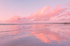 a beach with waves coming in to the shore and pink clouds above it at sunset