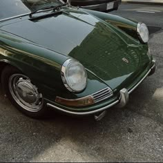 an old green car parked on the side of the road next to another car with it's hood up