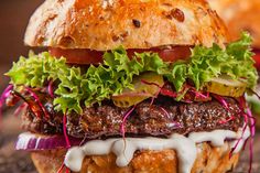 a hamburger with meat, lettuce and tomato on it sitting on a wooden table