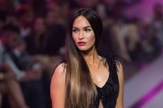 a woman with long hair walking down a runway