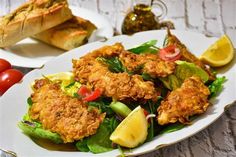 a white plate topped with fried chicken next to a salad and baguette bread