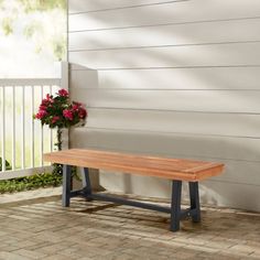 a wooden bench sitting on top of a brick floor next to a white fence and flowers