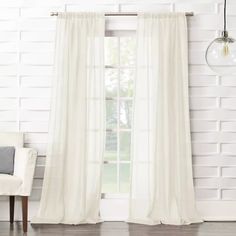 a white curtain hanging in front of a window next to a chair and light bulb