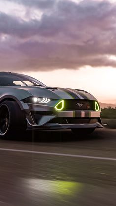 a sports car driving down the road at night with its headlights on and foggy clouds in the background