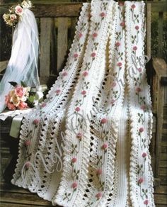 a white crocheted blanket sitting on top of a wooden bench next to flowers